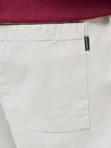 Bermuda de calce relajado color beige, con cintura elástica con cordón de ajuste, bolsillos delanteros y traseros, confeccionada en tejido dobby con textura sutil y un toque de elasticidad.