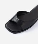Sandalia mule plana de cuero color negro, con diseño minimalista, capellada ancha y punta cuadrada.