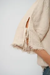 Blusa beige de lino con mangas 3/4 con lazos y detalle de flecos en los puños.