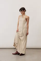 Vestido largo beige con cuello halter y detalle drapeado en la parte frontal.