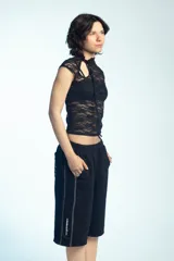 Musculosa de encaje negro con cuello alto, detalles de tiras para anudar y mangas cortas ajustadas.