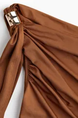 Top color marrón de punto elástico, con un hombro descubierto y una tira larga que cae desde el hombro. Presenta fruncidos en los laterales para un efecto drapeado.