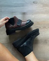 Botas tipo chelsea de cuero vacuno en combinación de colores marrón y negro, con suela track dentada y elásticos laterales.