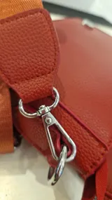 Cartera tipo bandolera de tamaño pequeño, color rojo, con solapa frontal y letras doradas estampadas que dicen 'THE MINI BAG'. Incluye una correa de tela ajustable y herrajes metálicos.