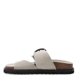 Sandalias Miss Carol modelo Melak de color beige, con tira ancha ajustable mediante una hebilla metálica grande y presilla para el dedo. Cuenta con suela de corcho y base de goma negra.