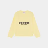 Sweater de punto color amarillo pálido, con cuello redondo y manga larga, corte oversize. Presenta un estampado central con el texto "EME STUDIOS" en mayúsculas y debajo "curated by ben ice" en cursiva.