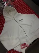 Hoodie de color blanco con capucha, diseño de corte holgado y estampado gráfico en la espalda con tipografía negra.