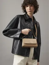Cartera bandolera Calvin Klein color beige con monograma en relieve. Tiene correa ajustable, cierre de cremallera y logo de la marca en el frente.