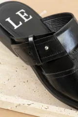 Sandalias tipo mule de cuero marrón con puntera cuadrada, diseño abierto y hebilla ajustable.