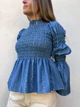 Blusa azul de manga larga con cuello alto y diseño fruncido tipo nido de abeja en el torso y las mangas, con sutiles detalles estampados.