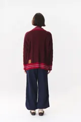 Buzo de tejido de punto con diseño de trenzas, color crema con detalles en marrón en cuello, puños y ruedo. Presenta líneas finas en contraste y pequeñas costuras decorativas en forma de cruz.