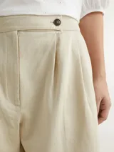 Pantalón beige de pierna ancha confeccionado en sarga de mezcla de algodón orgánico, lyocell y lino. Presenta pinzas en la parte delantera, cierre de cremallera con botón y logo de Tommy Hilfiger bordado en la parte trasera.