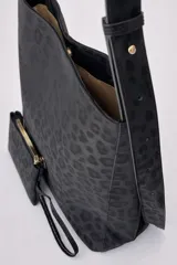 Bolso tipo hobo con estampado animal print en tonos negros, confeccionado en material sintético. Cuenta con una correa larga regulable, cierre superior y un mini monedero desmontable a juego.