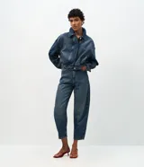 Pantalón de jean modelo carrot con cintura alta, corte holgado en caderas y piernas que se estrechan hacia el tobillo. Confeccionado en denim de algodón con lavado medio, cuenta con cinco bolsillos funcionales, cierre frontal con botón y cremallera, y trabillas para cinturón.