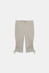 Pantalón capri de tiro medio con efecto lavado, bolsillos delanteros y traseros, y bajo con frunces laterales ajustables mediante cordones.