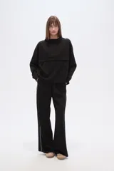 Buzo negro de corte holgado con capucha, manga larga y bolsillo frontal tipo canguro. Presenta un diseño minimalista con una solapa frontal sobre el pecho.