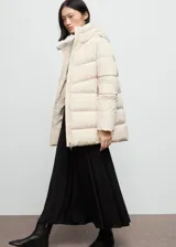 Campera acolchada de corte recto y diseño puffer, color beige, con capucha, cuello alto y cierre frontal de cremallera doble. Cuenta con mangas largas con puños elásticos y dos bolsillos laterales con cierre.