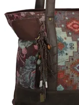 Cartera tipo tote con diseño patchwork que combina paneles de tejido con motivos geométricos y florales, con detalles en cuero sintético marrón en la base y las asas. Incluye un llavero decorativo con borlas y cuentas colgando de una de las asas.