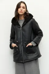 Campera tipo gamulán de cuero sintético negro con interior forrado en corderito sintético. Presenta capucha, cierre frontal con cremallera, bolsillos frontales tipo parche y cordones ajustables en la cintura.