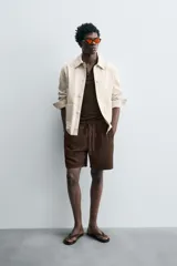 Bermuda de algodón color beige claro, de corte regular fit, con cintura elástica ajustable mediante cordón. Presenta bolsillos laterales y un bolsillo trasero de vivo.