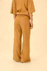 Pantalón de lino color mostaza, de corte wide leg, con sutil estampado floral en la parte inferior de la pierna izquierda y botón a la vista en la cintura.