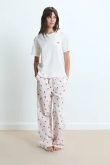 Pijama compuesto por una remera de cuello redondo en color blanco con un pequeño estampado de labios rojos en el pecho y un pantalón largo de corte holgado con estampado de rayas verticales y labios rojos sobre fondo claro.