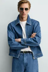 Cazadora de denim de algodón con cierre frontal de cremallera, cuello solapa y un bolsillo plastrón en el pecho. Presenta un diseño de corte regular con efecto lavado.