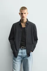 Camisa de corte relajado confeccionada en tejido de algodón con textura. Presenta cuello italiano, manga larga con puños abotonados y cierre frontal mediante botonadura.