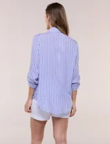 Camisa de corte clásico y silueta relajada con diseño de rayas verticales en azul y blanco, cuello camisero tradicional, cierre frontal con botones y bolsillo aplicado en el pecho con rayas horizontales. Cuenta con mangas largas con presillas para arremangar y ruedo redondeado.