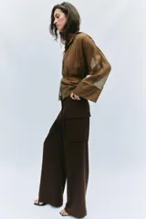 Pantalón cargo de tiro medio en color marrón oscuro, con corte recto y amplio. Presenta bolsillos laterales tipo cargo con solapa y detalle de pliegues frontales. Cierre frontal con cremallera y botón.
