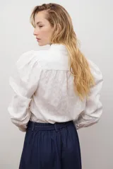 Camisa blanca de manga corta con cuello mao y volados, botones frontales y bordados de hojas y flores en color dorado.