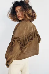 Cazadora marrón de efecto ante con cuello de solapa, cierre frontal de botones y bolsillos delanteros. Presenta detalles de flecos en el pecho y las mangas.
