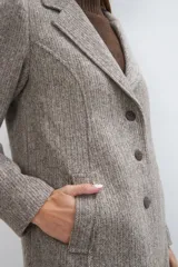 Saco corto entallado de lana fina, con cuello solapa, manga larga y cierre frontal con botones. Presenta un diseño clásico con textura de espiga en tonos tierra.