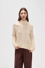 Polera de tejido de punto color crema, con cuello alto y diseño de trenzas verticales. Presenta mangas largas con puños acanalados y un corte holgado.