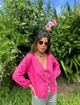 Blusa fucsia de lino con escote en V y mangas largas abullonadas con puños elásticos. Se cierra con lazos en la parte delantera.