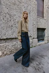 Jeans de mezclilla azul oscuro, tiro medio, corte pierna ancha (wide leg). Presenta bolsillos delanteros de parche con detalle de cadena metálica decorativa.