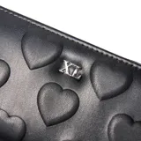 Billetera rectangular color negro con cierre perimetral y textura de corazones grabados en relieve. Incluye aplique metálico con las siglas XL en el centro.