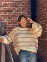 Buzo tejido de punto con silueta oversize, color crudo con rayas horizontales en color rosado. Presenta cuello redondo y mangas largas con caída relajada.