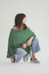 Poncho tejido de punto en color verde, con diseño holgado, cuello redondo y terminación con flecos en el ruedo.