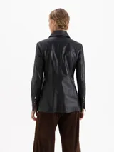 Parka de cuero vacuno color negro, con diseño utilitario que incluye bolsillos frontales con tapa y fuelle. Presenta un cuello con detalle de tachas metálicas y cierres en los puños.