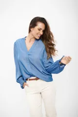 Camisa de tela liviana color azul medio, con cuello en V, mangas largas abullonadas y puños con elástico y volados.