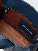 Cartera tipo tote de Marc Jacobs, confeccionada en cuero granulado color azul marino. Presenta el logo de la marca estampado en el frente, doble asa superior y correa ajustable y extraíble para llevar al hombro o cruzada.