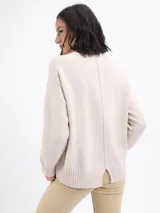Buzo de punto color beige, con cuello alto y mangas largas con puños acanalados.