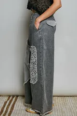 Pantalón de jean gris oscuro con corte holgado, parches asimétricos estilo patchwork con estampados de rayas y animal print en las rodillas, y detalle de tira central con botones a presión y encaje.