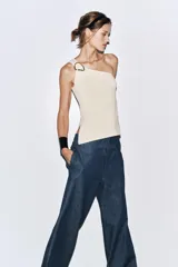 Top blanco de punto con escote asimétrico y aplique metálico dorado en el hombro.