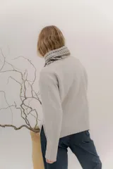 Polera tejida en lambswool color beige, con cuello alto y diseño de intarsia en tonos marrones y grises. Presenta botones forrados en el cuello para modular la apertura.