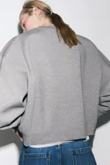 Sudadera gris de cuello redondo y manga larga, con puños y dobladillo acanalados.