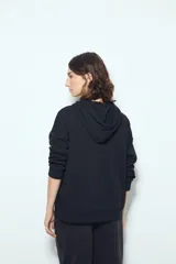 Canguro negro de calce relajado con capucha y cordones ajustables. Presenta un estampado gráfico frontal de un ojo con rayos de sol y la frase "STAY WEIRD".