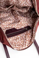 Bolso tipo tote de gran tamaño en color bordó, confeccionado en material sintético con textura de gamuza. Cuenta con cierre superior, correas largas de hombro en tono marrón oscuro y una placa metálica decorativa en el frente.