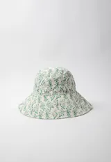 Gorro tipo bucket hat estampado con flores y hojas en tonos verde y celeste sobre fondo blanco. Es reversible.